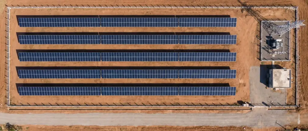 Labelled aerial view of a fixed-tilt one megawatt solar plot: five module rows with wide bare-earth row spacing, a setback strip inside the fence line, a switchyard and inverter station at one end, and an internal access road along the front