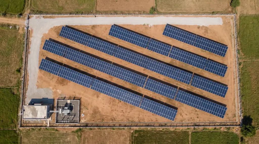Aerial view of a ground-mounted solar power plant with fixed-tilt rows, an inverter room and a small fenced switchyard
