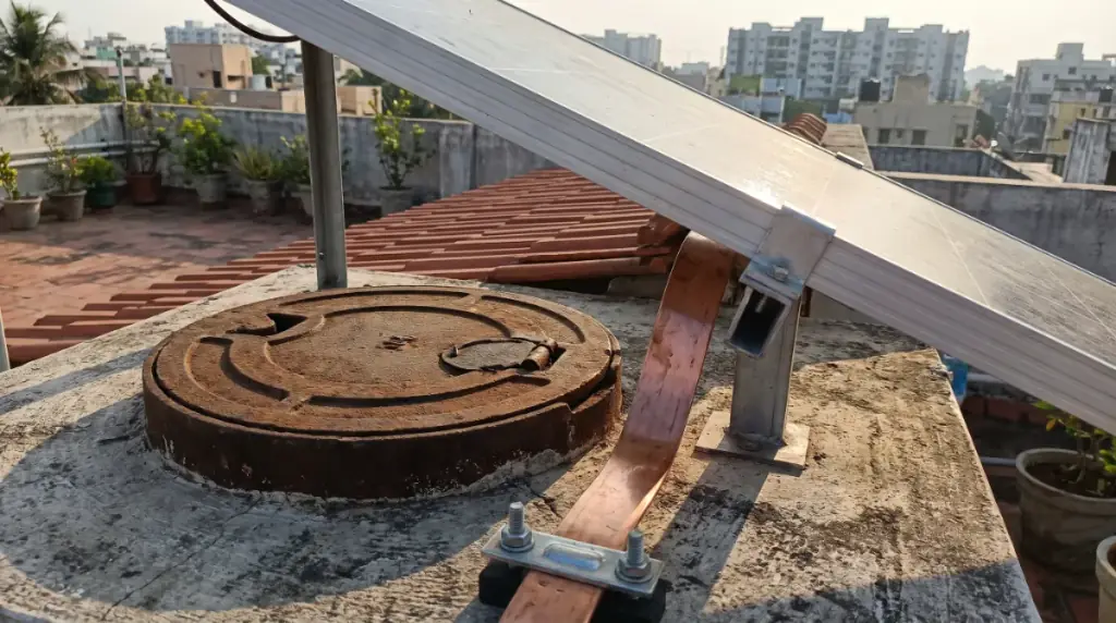 An earthing pit lid and copper earthing strip beside a rooftop solar structure leg, rooftop solar in Ekkattuthangal