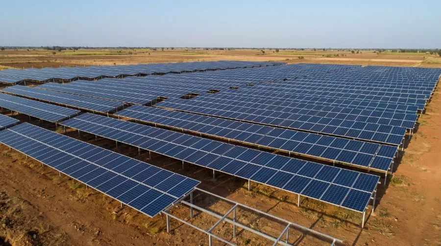 Rows of fixed-tilt solar panels all set at the same angle on low steel frames over bare earth