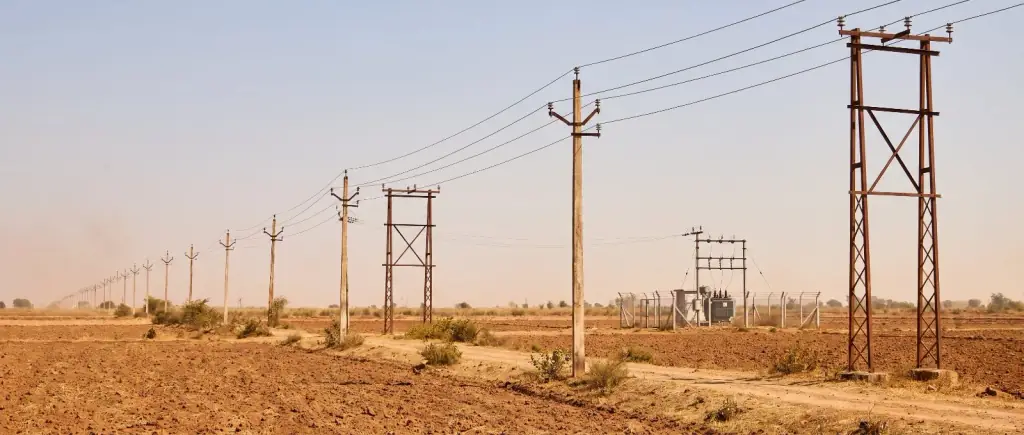 A 33 kV overhead line on concrete and lattice poles running across farmland to a small fenced rural distribution substation