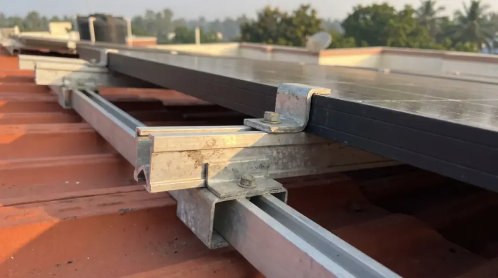 A close-up of galvanised mounting clamps and rails holding the edge of a dark solar module, rooftop solar in Tamil Nadu