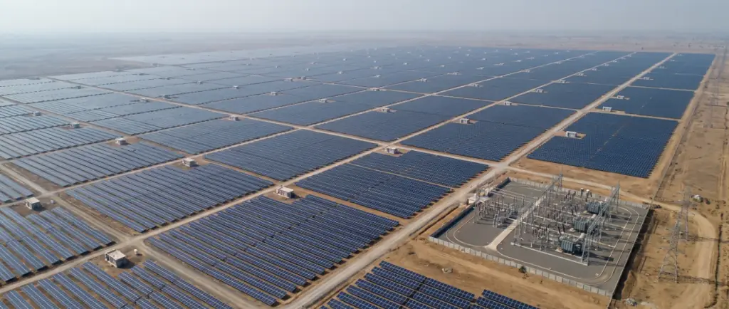 High aerial view of a large solar plant with geometric blocks of panel rows, internal roads, several inverter stations and a substation